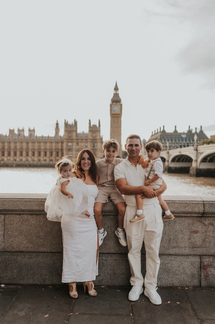 A family in cream and beige outfits beside the Thames with Big Ben rising behind them during their London family photoshoot.