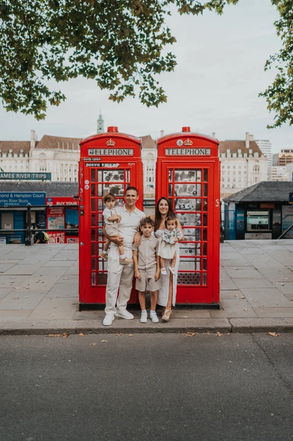 Three children standing together in front of red telephone boxes near Westminster Pier during their London family photoshoot.