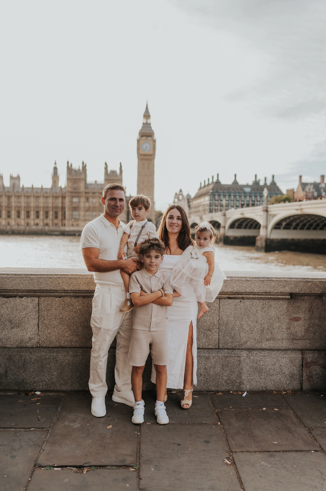 Parents standing with their three children beside the Thames with Big Ben across the water during their London family photoshoot.