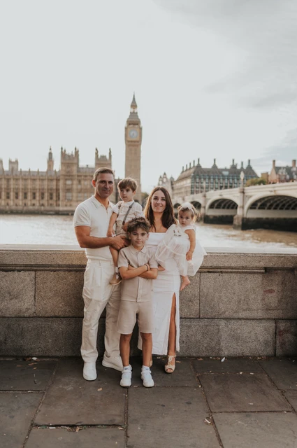 London family photoshoot: together beside the Thames and Big Ben Parents standing with their three children beside the Thames with Big Ben across the water during their London family photoshoot.