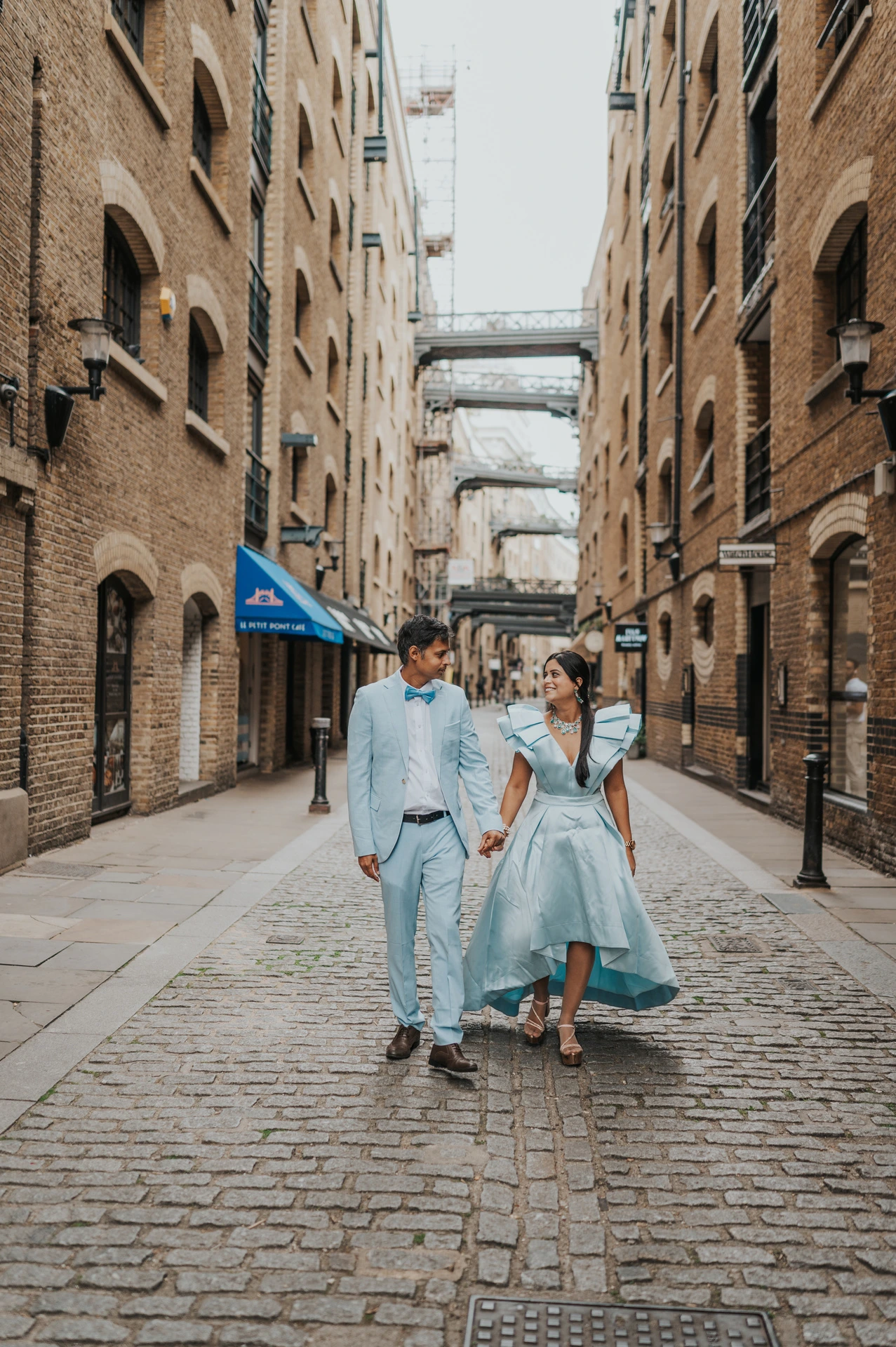 A couple walking hand in hand through a cobbled lane beside Butler’s Wharf during their London family photoshoot.