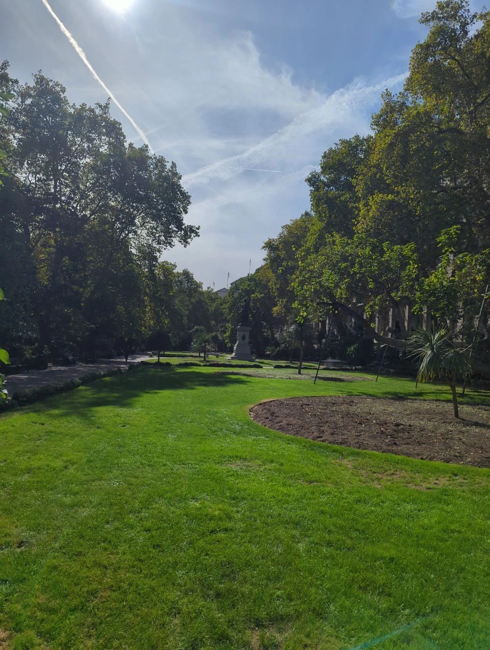 Mature trees, planted beds, lawns and a statue in Whitehall Gardens on a sunny day