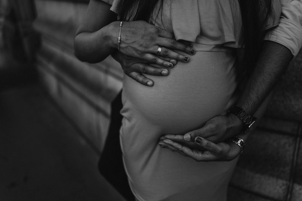 London maternity photoshoot: black-and-white detail of hands around her bump. In black and white, a close detail shows the couple’s hands resting above and beneath her bump beside the Tower Bridge wall during their London maternity photoshoot.