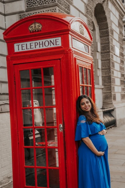 London maternity photoshoot at the corner of a red telephone box The expectant mother rests her hands on her bump beside an angled red telephone box during a London maternity photoshoot.