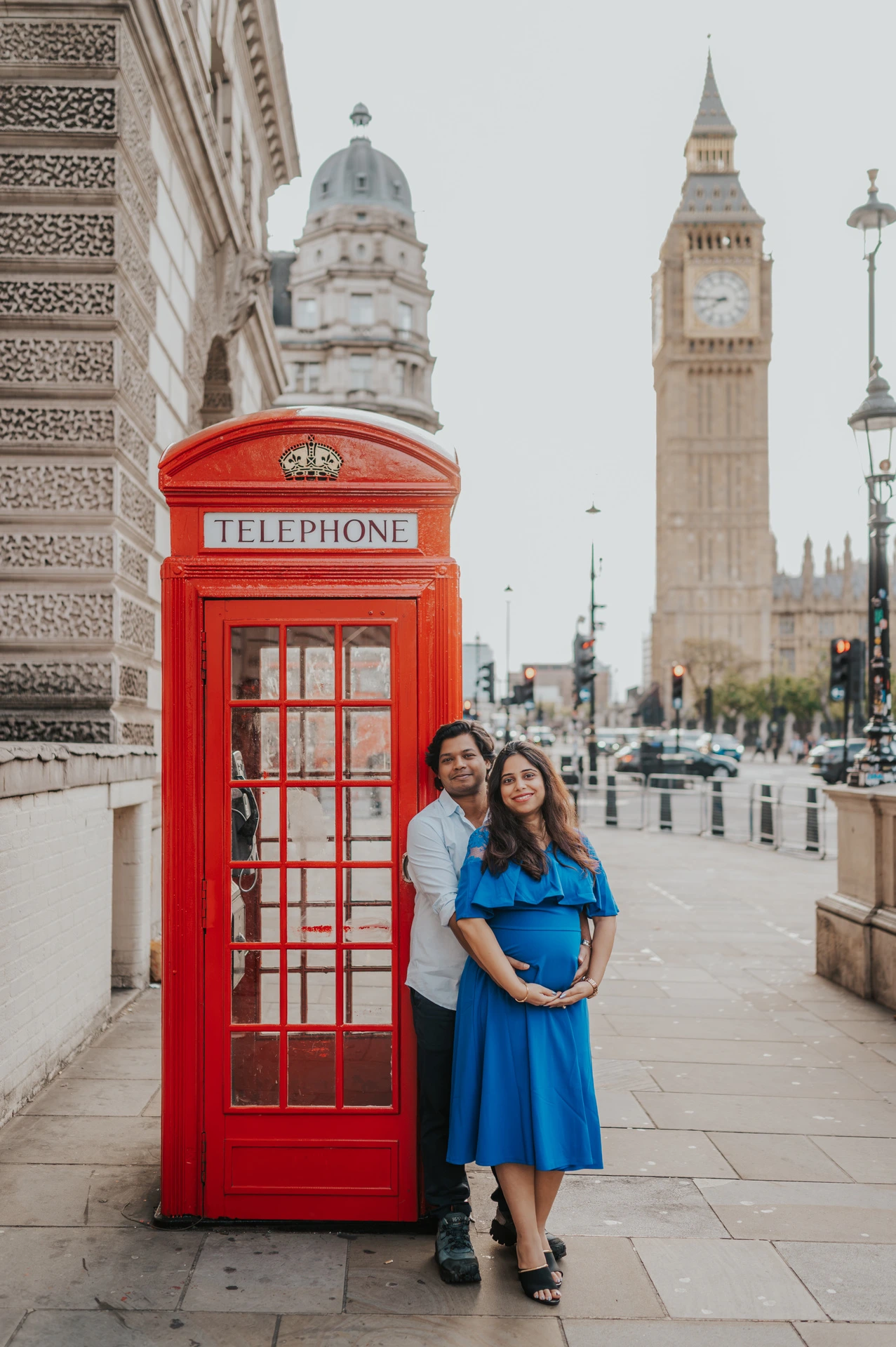 The couple face the camera beside a red telephone box, with Big Ben behind them, during a London maternity photoshoot.