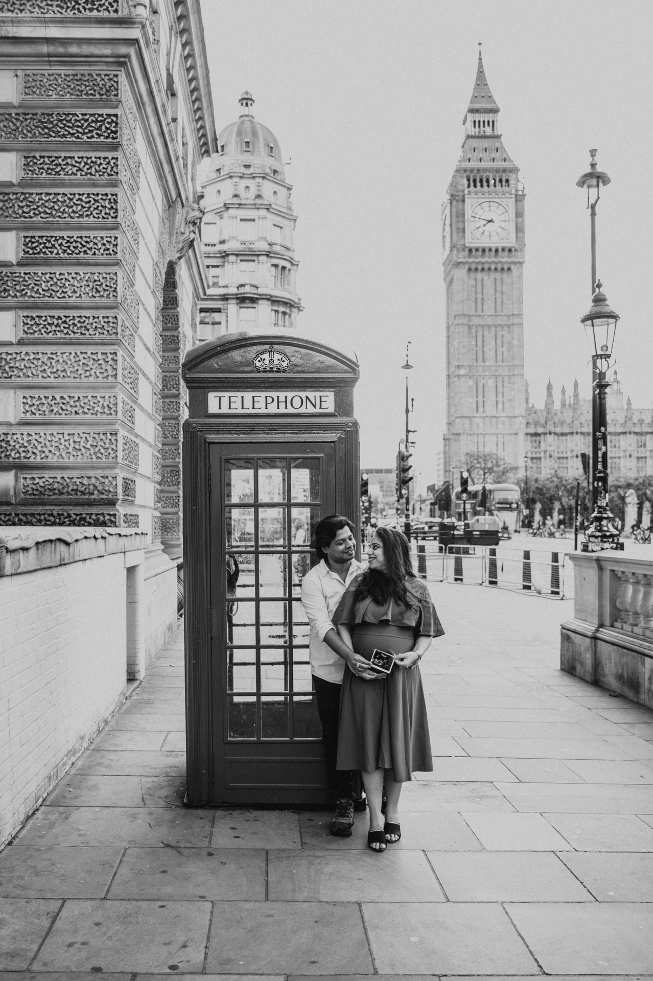 Black-and-white portrait of the couple beside a telephone box with Big Ben behind them during a London maternity photoshoot.