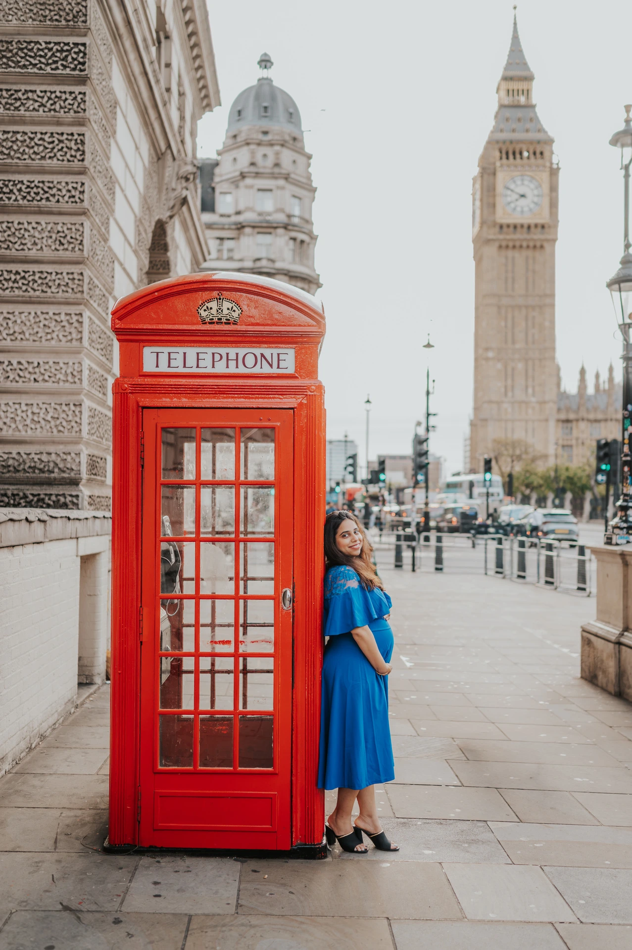 The expectant mother looks towards the camera beside a red telephone box with Big Ben in view during a London maternity photoshoot.