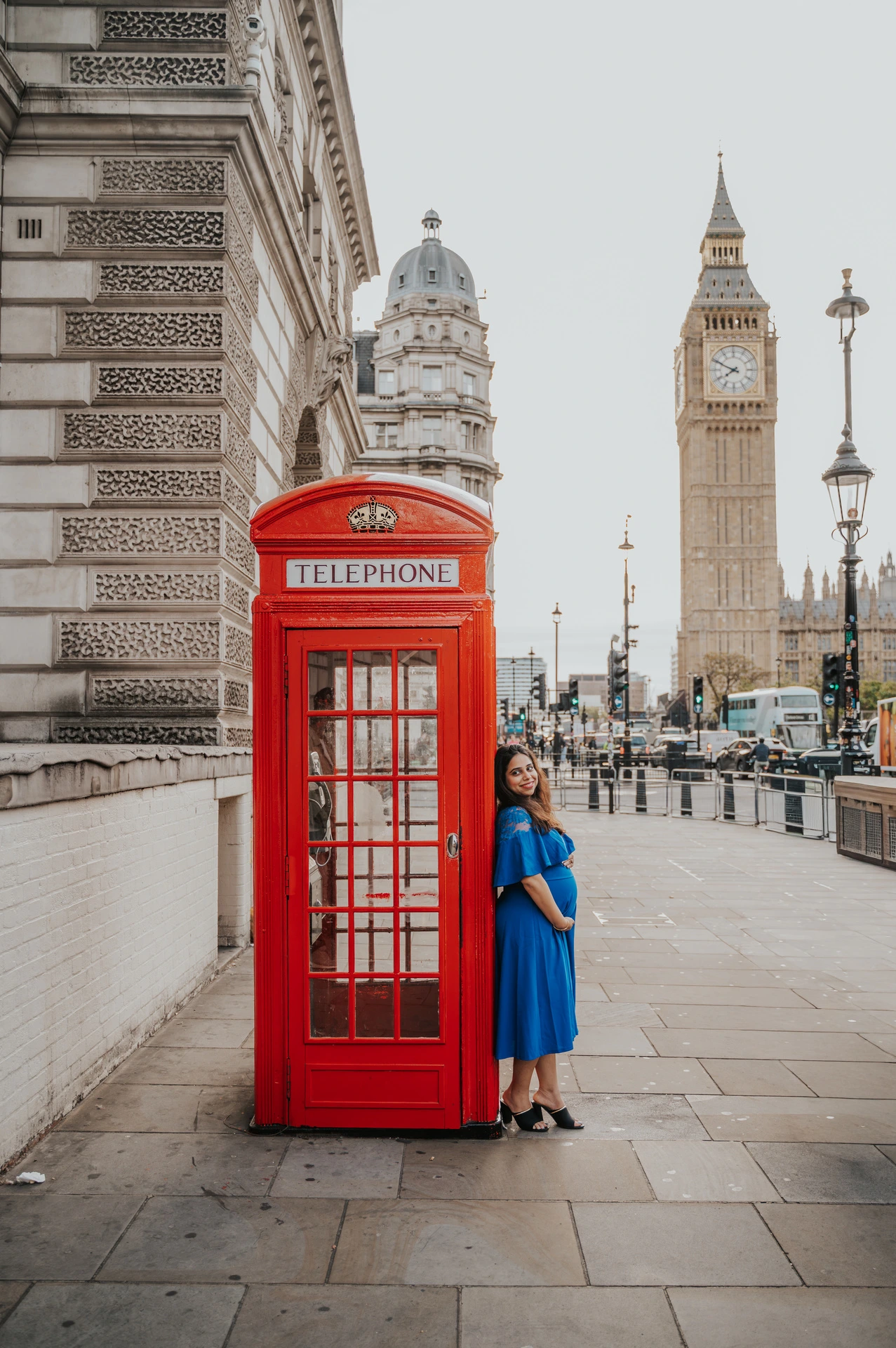 The expectant mother stands beside a red telephone box below the view of Big Ben during a London maternity photoshoot.