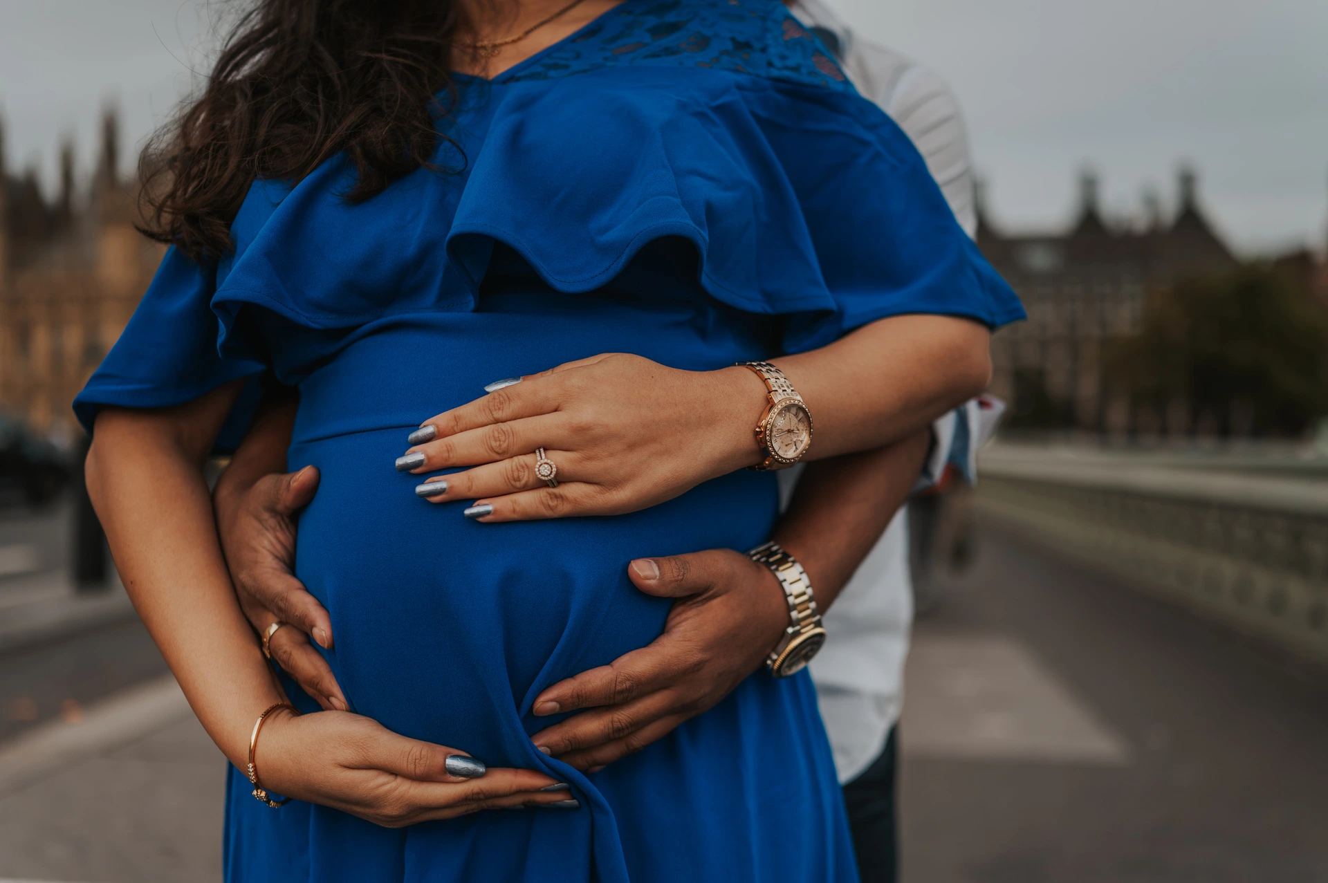 London maternity photoshoot with a close-up of hands around the bump Close-up of the couple's hands around the baby bump and blue dress during a London maternity photoshoot on Westminster Bridge.