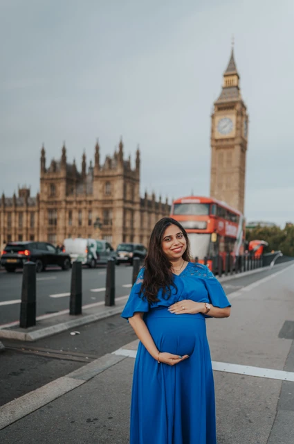 London maternity photoshoot with a blue dress and Big Ben The expectant mother rests her hands above and below her bump with Big Ben and a red bus behind her during a London maternity photoshoot.