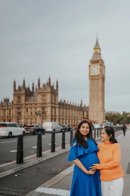 The expectant mother in blue stands beside a woman in orange, with their hands on her bump and Big Ben behind, during a London maternity photoshoot.