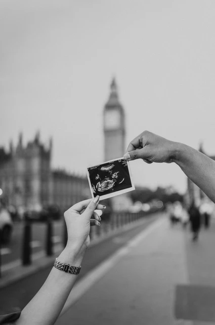 Black-and-white close-up of hands holding an ultrasound scan with Big Ben blurred behind during a London maternity photoshoot.