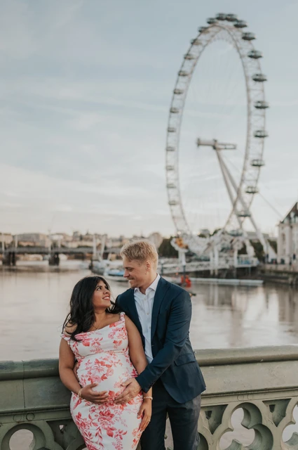 A close London Eye portrait at a London maternity photoshoot Close portrait of the couple smiling at each other above her bump, with the London Eye behind, during their London maternity photoshoot.