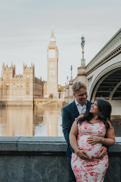 A bump portrait beside the Thames at a London maternity photoshoot Close portrait of the couple cradling her bump beside the river, with Big Ben and Westminster Bridge behind, during their London maternity photoshoot.