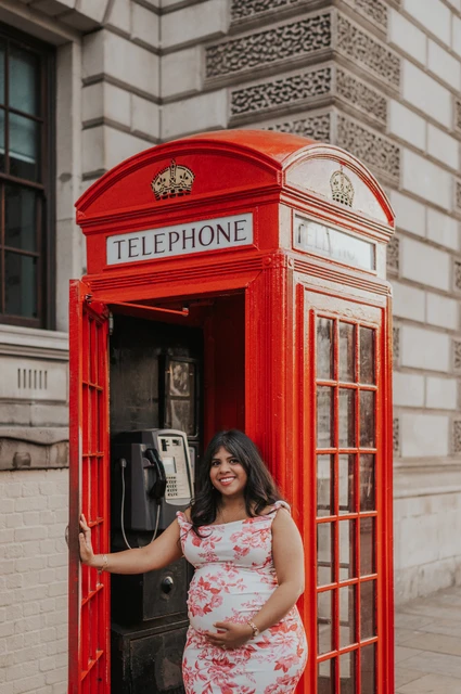 London maternity photoshoot portrait at an open telephone box Closer portrait of the mother-to-be smiling at the open red telephone box door during her London maternity photoshoot.