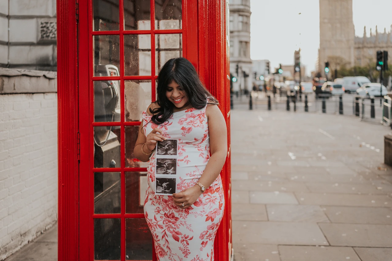 A personal ultrasound moment in a London maternity photoshoot Landscape portrait of the mother-to-be looking down at her ultrasound scan in front of a red telephone box during her London maternity photoshoot.