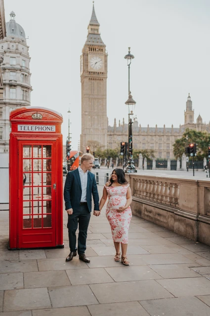 A walk past Big Ben during a London maternity photoshoot The expectant couple walking hand in hand past a red telephone box, with Big Ben in view, during their London maternity photoshoot.