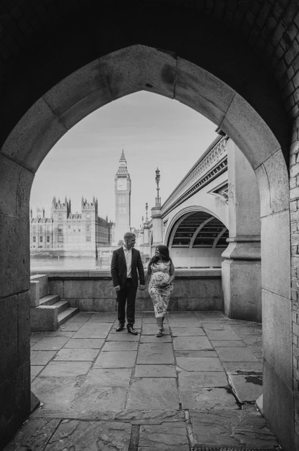 A black-and-white Westminster arch portrait at a London maternity photoshoot Black-and-white portrait of the couple walking beneath the stone arch beside Westminster Bridge during their London maternity photoshoot.