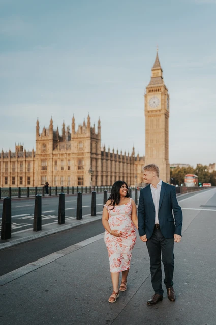 A Westminster Bridge walk at a London maternity photoshoot The couple walking hand in hand on Westminster Bridge with Big Ben and the Houses of Parliament behind them during their London maternity photoshoot.