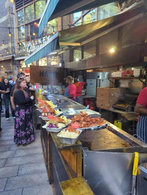 Hot food on a Borough Market counter with stallholders and visitors behind it