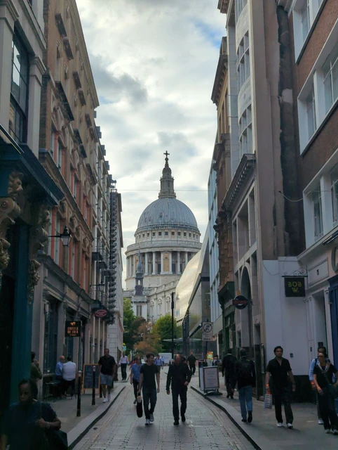The dome of St Paul’s Cathedral seen along a narrow street with pedestrians and shopfronts