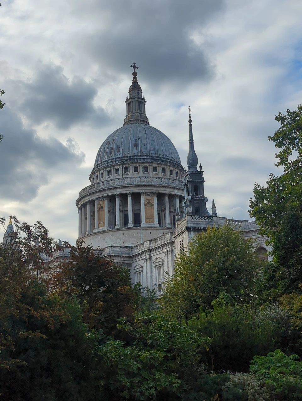 St Paul’s Cathedral dome above trees and shrubs under a cloudy London sky