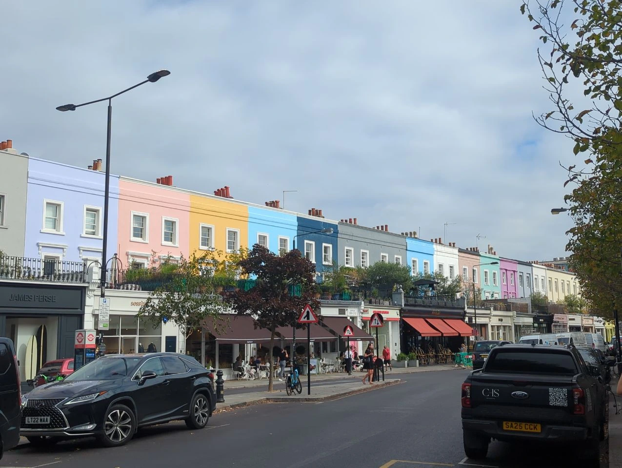 Pink, yellow and blue façades above shops along a Notting Hill street with passing traffic