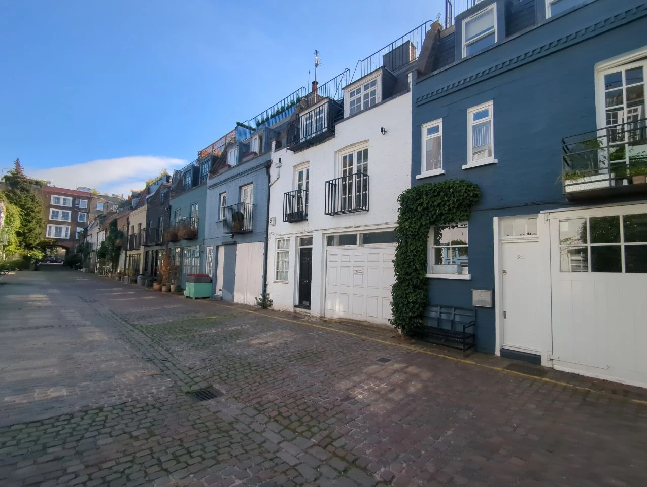 Painted homes, potted plants and climbing greenery beside a cobbled Notting Hill mews