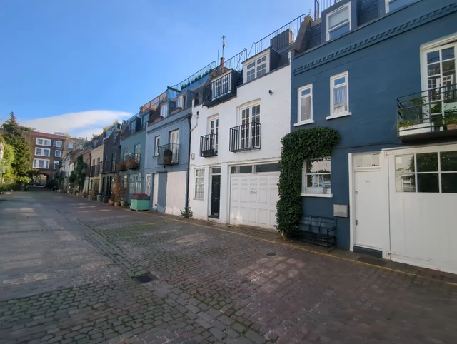 Painted homes, potted plants and climbing greenery beside a cobbled Notting Hill mews
