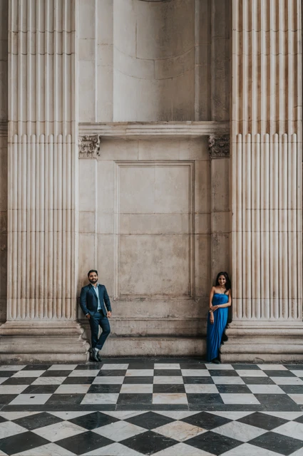 London proposal photoshoot: columns and checkerboard paving The couple standing apart between the tall columns of St Paul’s Cathedral above a checkerboard floor during their London proposal photoshoot.