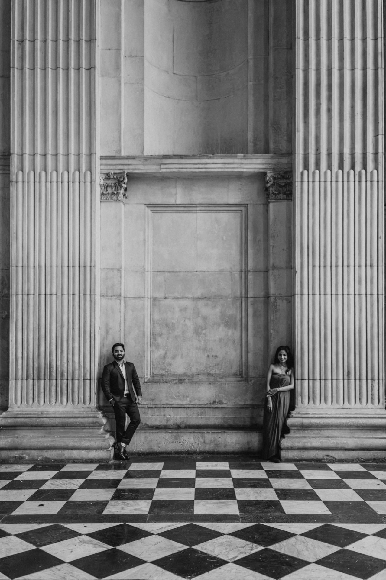 Black-and-white photograph of the couple between the tall stone columns of St Paul’s Cathedral with the checkerboard floor below during their London proposal photoshoot.