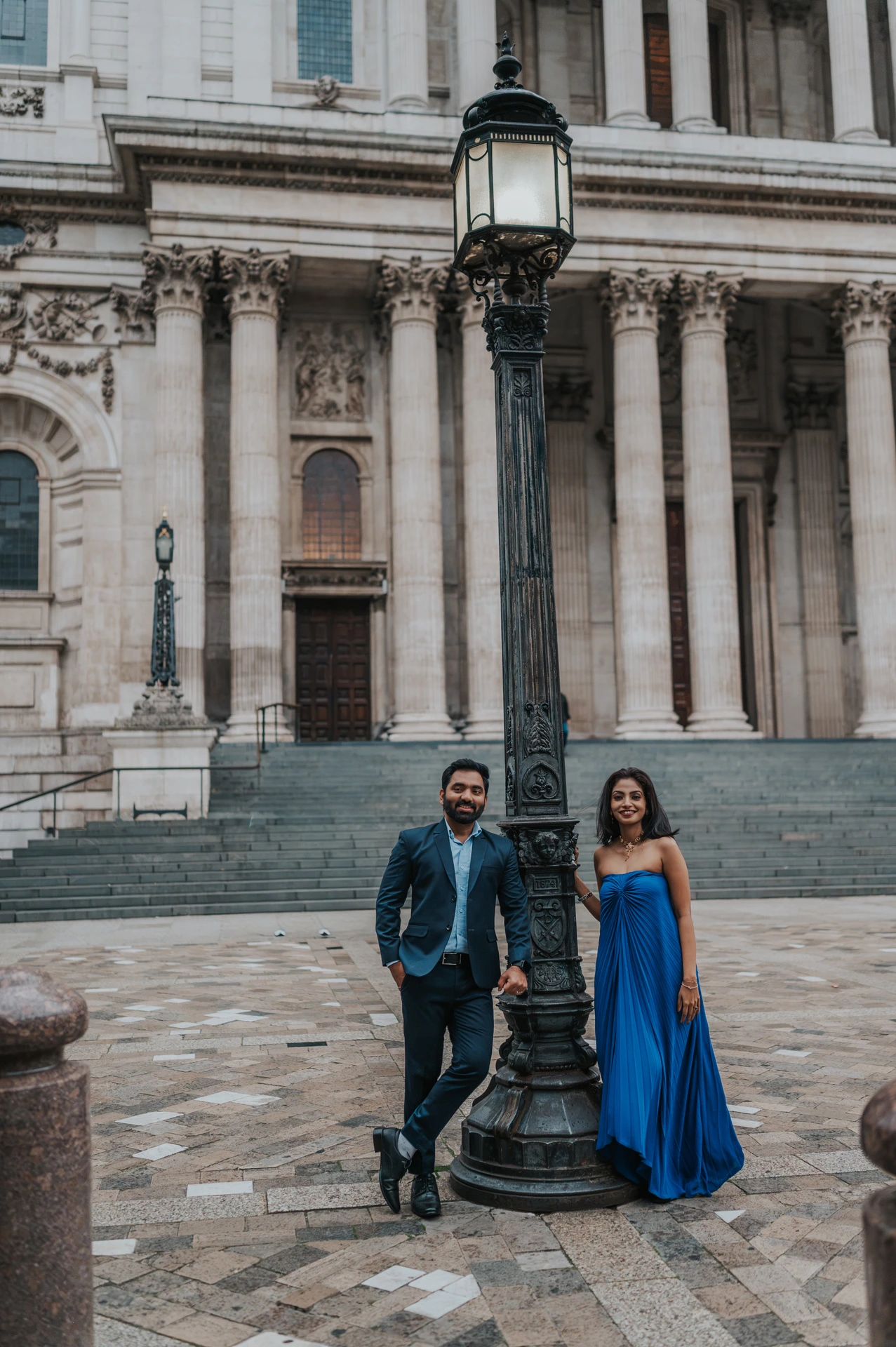 The couple beside a traditional lamp post in front of the columns and steps of St Paul’s Cathedral during their London proposal photoshoot.