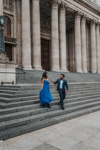 London proposal photoshoot: a blue dress on the cathedral steps The couple walking together on the cathedral steps, with her long blue dress against the pale stone during their London proposal photoshoot.