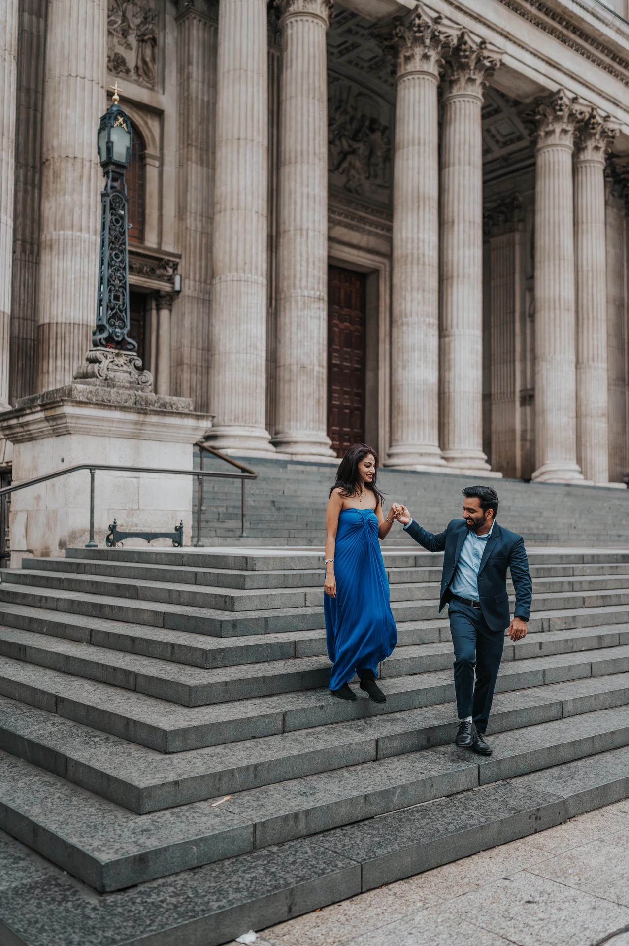 The couple holding hands while descending the stone steps outside St Paul’s Cathedral during their London proposal photoshoot.