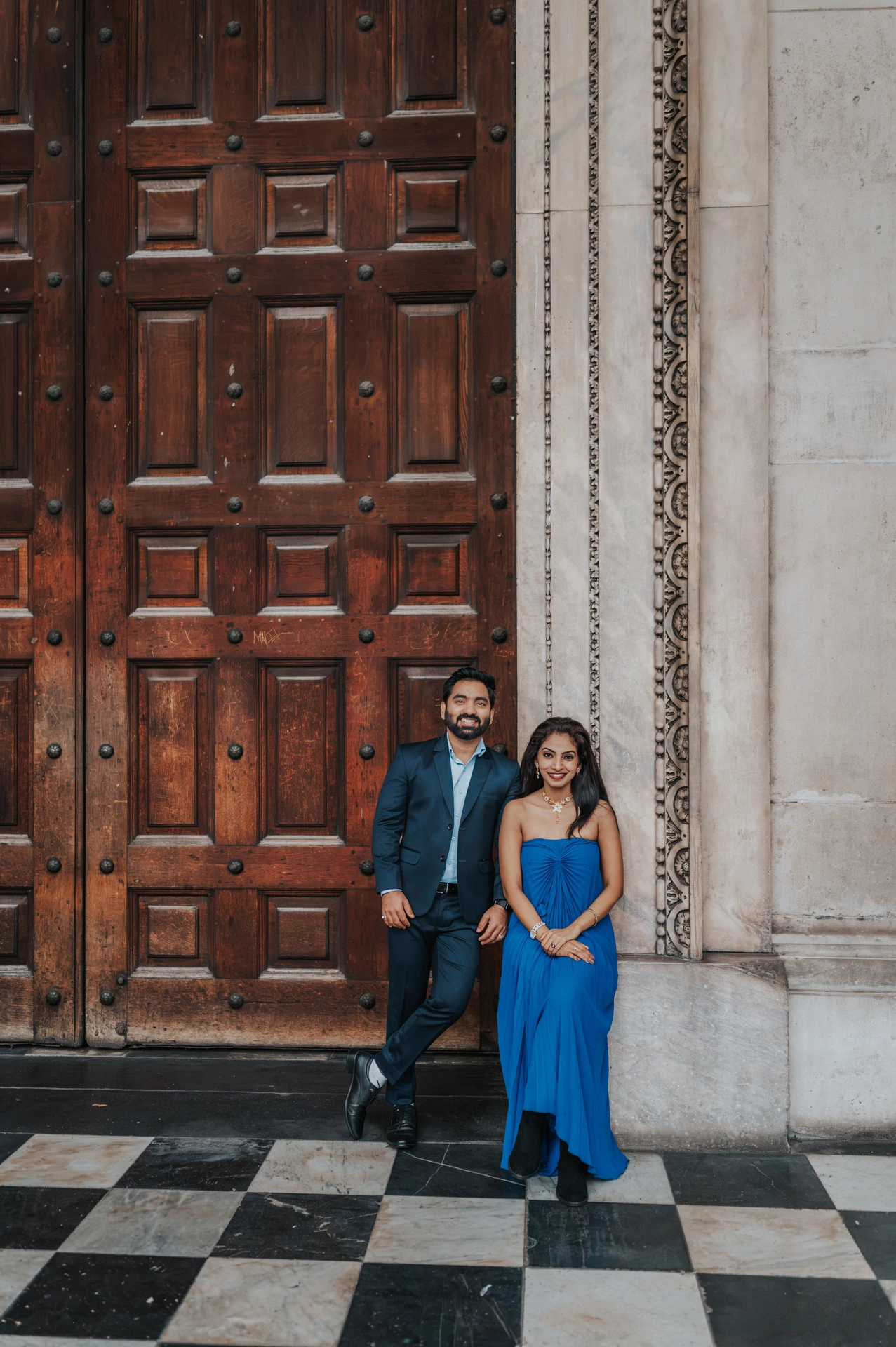 The couple together beside the tall wooden doors and checkerboard paving at St Paul’s Cathedral during their London proposal photoshoot.