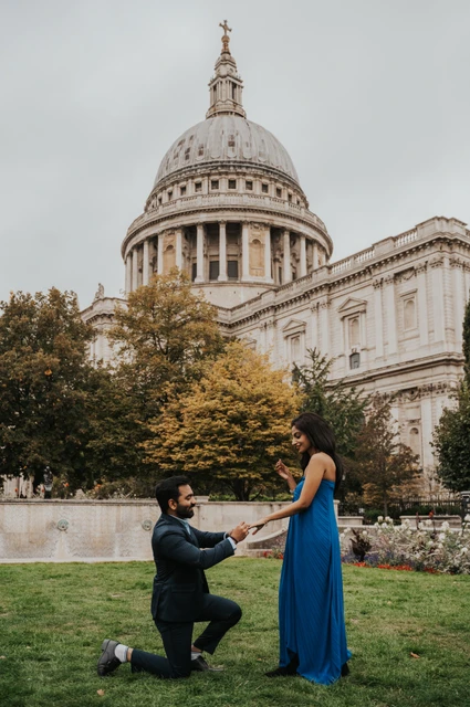 London proposal photoshoot: a proposal beneath St Paul’s Cathedral A man kneeling and holding his partner’s hand on the Festival Gardens lawn beneath St Paul’s Cathedral during their London proposal photoshoot.