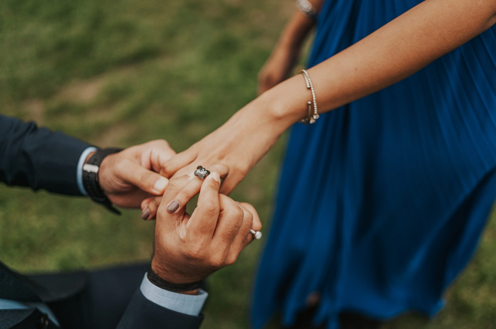 A close view of the engagement ring being placed on the woman’s hand, with her blue dress in the background during their London proposal photoshoot.