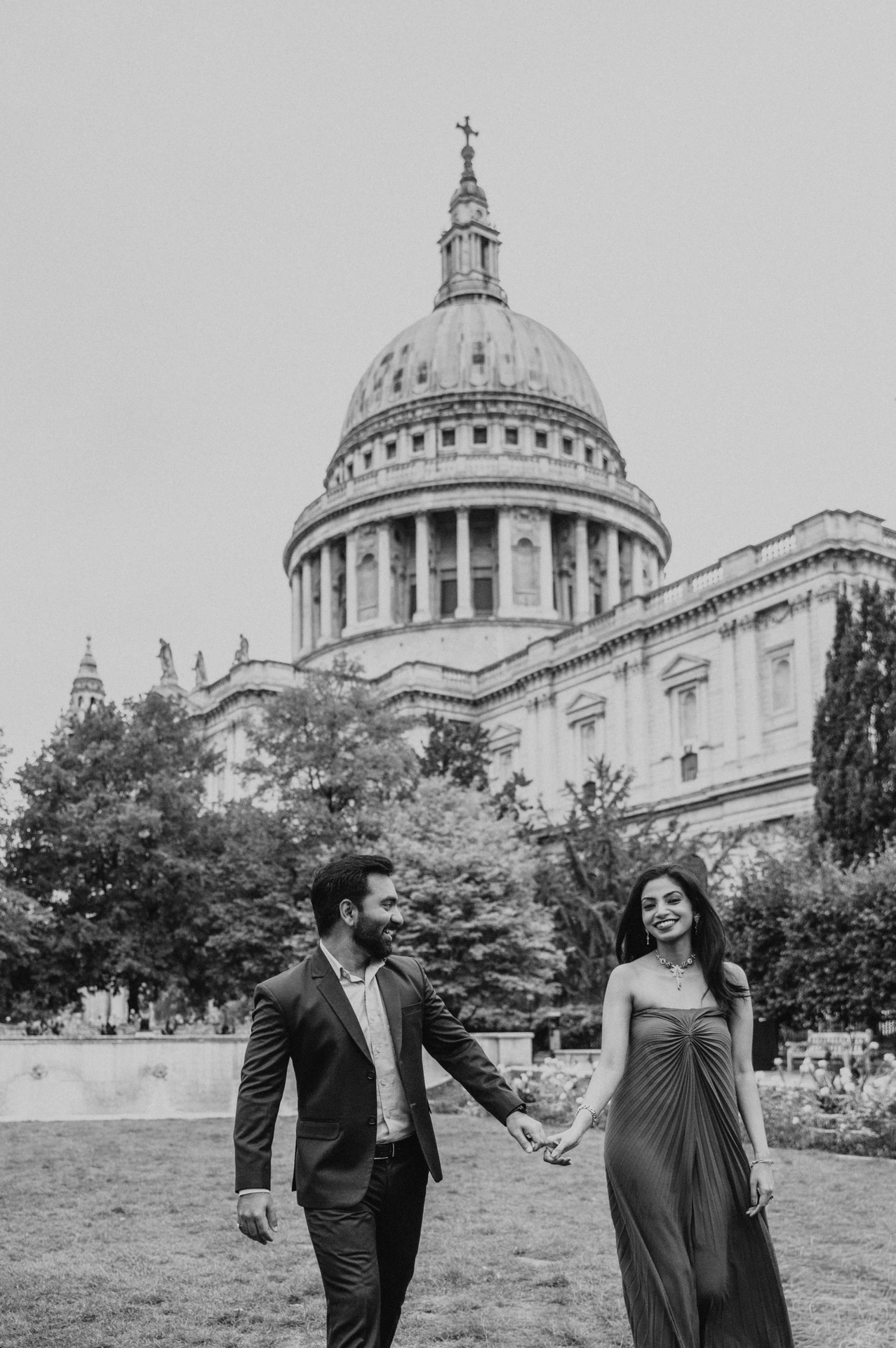 Black-and-white photograph of the couple walking hand in hand beneath St Paul’s Cathedral in Festival Gardens during their London proposal photoshoot.