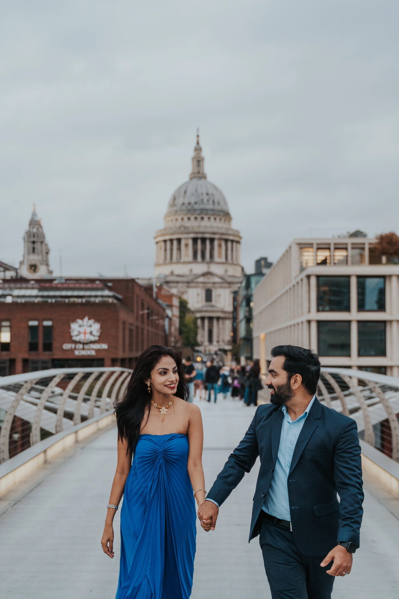 The couple walking hand in hand on Millennium Bridge, with St Paul’s Cathedral above the bridge railings during their London proposal photoshoot.