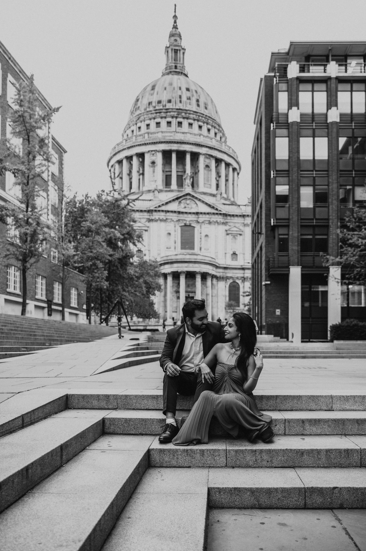 Black-and-white photograph of the couple sitting on the stone steps at Peter’s Hill with the dome of St Paul’s Cathedral behind them during their London proposal photoshoot.