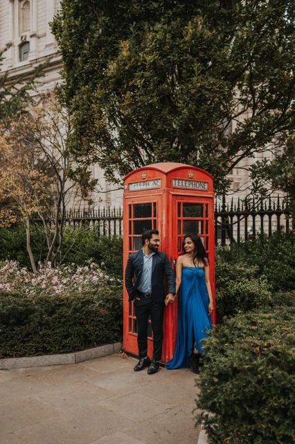 The couple standing together at a red telephone box surrounded by garden trees near St Paul’s Cathedral during their London proposal photoshoot.