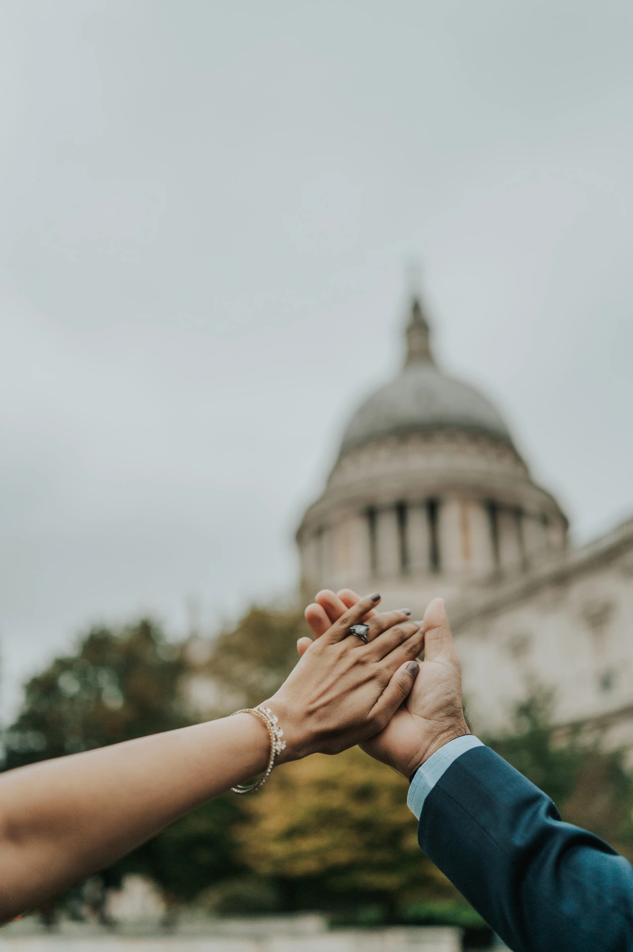 The couple raising their joined hands and showing the engagement ring with St Paul’s Cathedral softly in the background during their London proposal photoshoot.