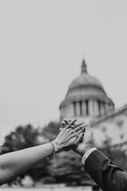 London proposal photoshoot: raised hands in black and white Black-and-white photograph of the couple’s raised hands and engagement ring against a softly framed view of St Paul’s Cathedral during their London proposal photoshoot.