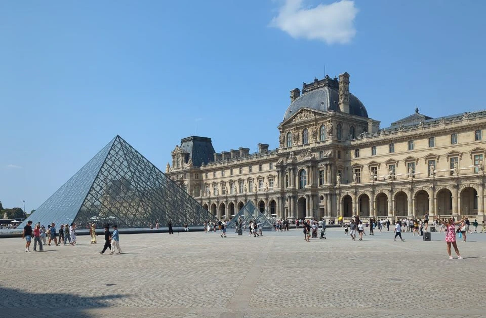 The Louvre Pyramid and palace arcades frame a broad sunlit courtyard in Paris, offering an architectural photoshoot backdrop.