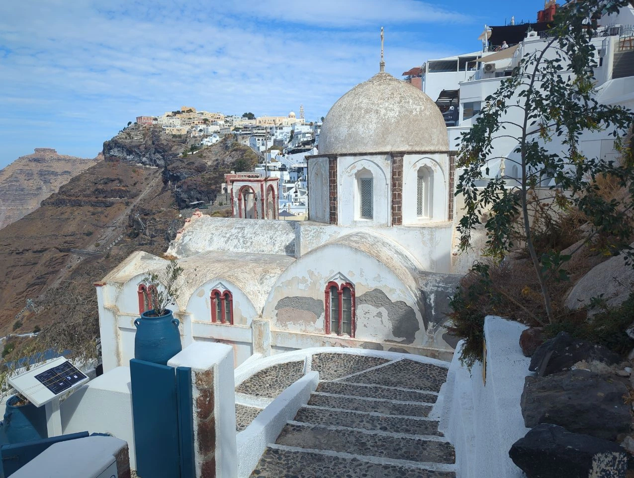 Lower Fira church and Skaros Rock | Santorini photo spots Weathered white church beside descending steps in lower Fira, with Skaros Rock and the upper town behind it