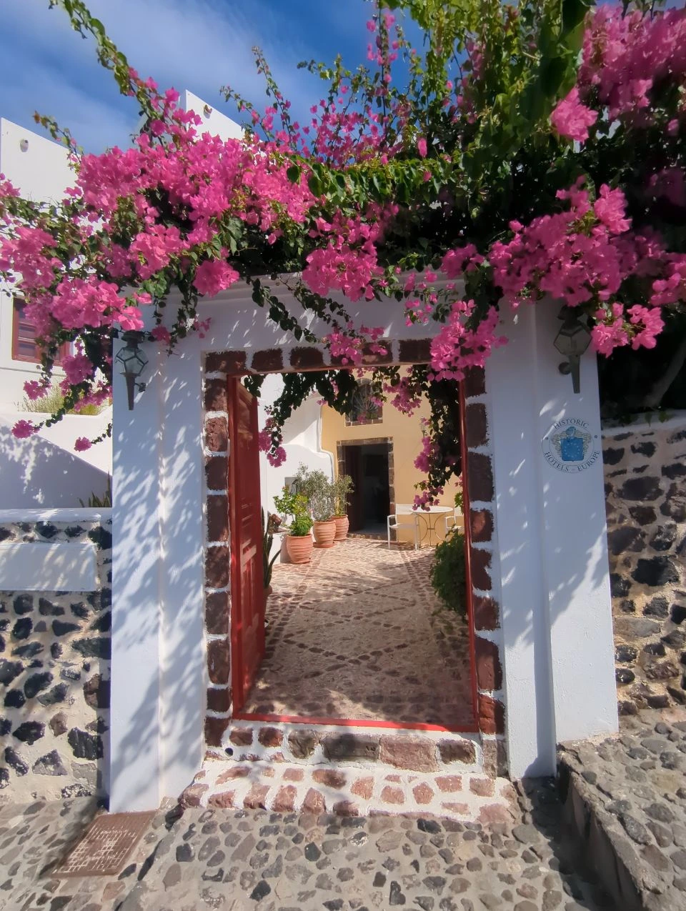 Red doorway and bougainvillea in lower Fira | Santorini Red hotel doorway beneath pink bougainvillea on a lower Fira lane