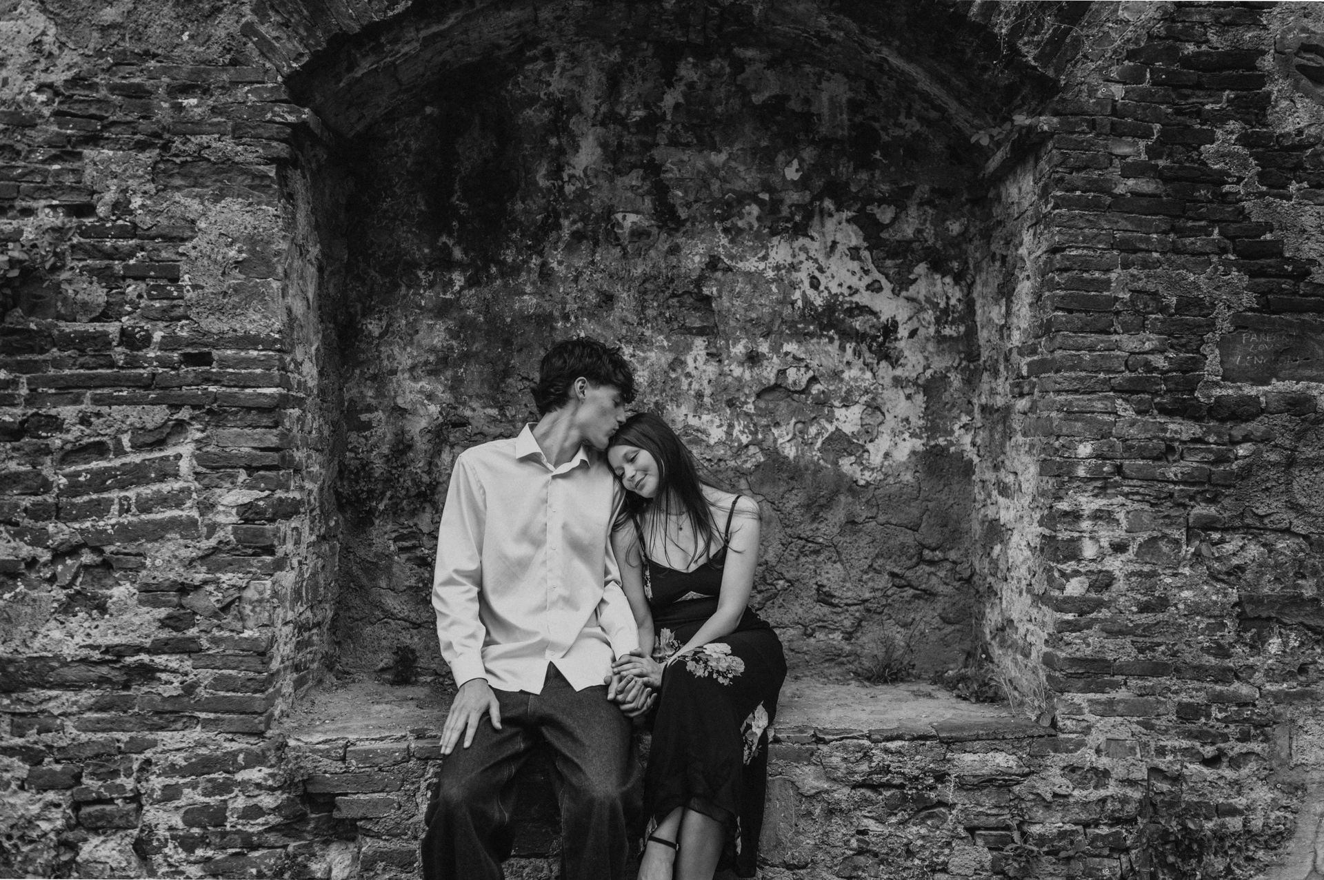 Black-and-white photograph of Alice leaning towards Pablo as they sit in an old brick alcove. From Alice and Pablo’s Lucca anniversary photoshoot.