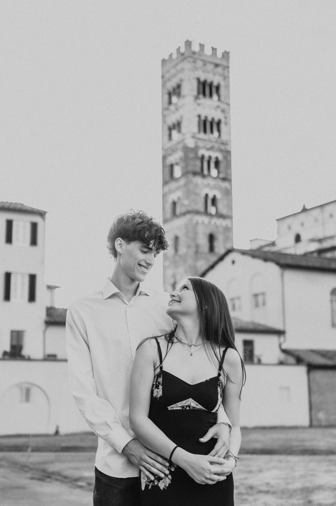 Black-and-white portrait of Alice and Pablo smiling at one another with San Martino’s bell tower behind them. From Alice and Pablo’s Lucca anniversary photoshoot.