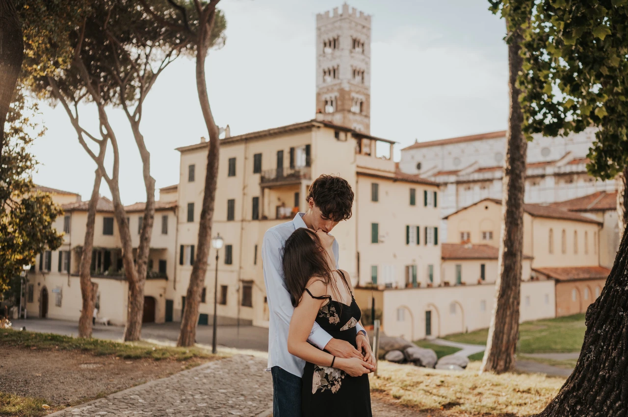 An anniversary photoshoot by Lucca’s Duomo di San Martino Alice and Pablo share a kiss beneath the trees, with the Duomo di San Martino rising behind them. From Alice and Pablo’s Lucca anniversary photoshoot.