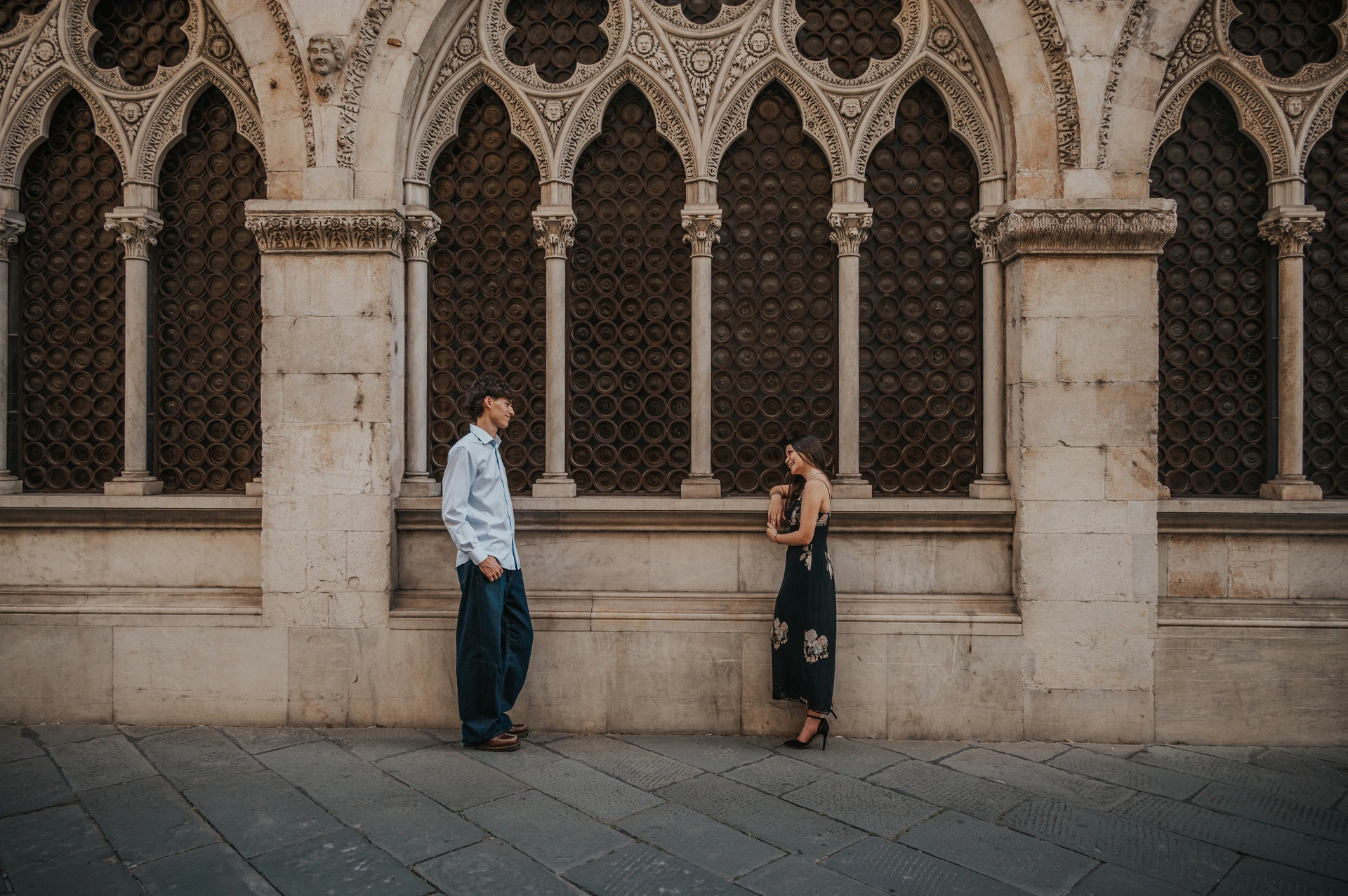 Wide photograph of Alice and Pablo holding hands beneath a row of carved Gothic arches. From Alice and Pablo’s Lucca anniversary photoshoot.